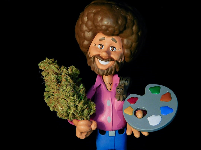 Cartoon Bob Ross figurine holding a hemp bud.